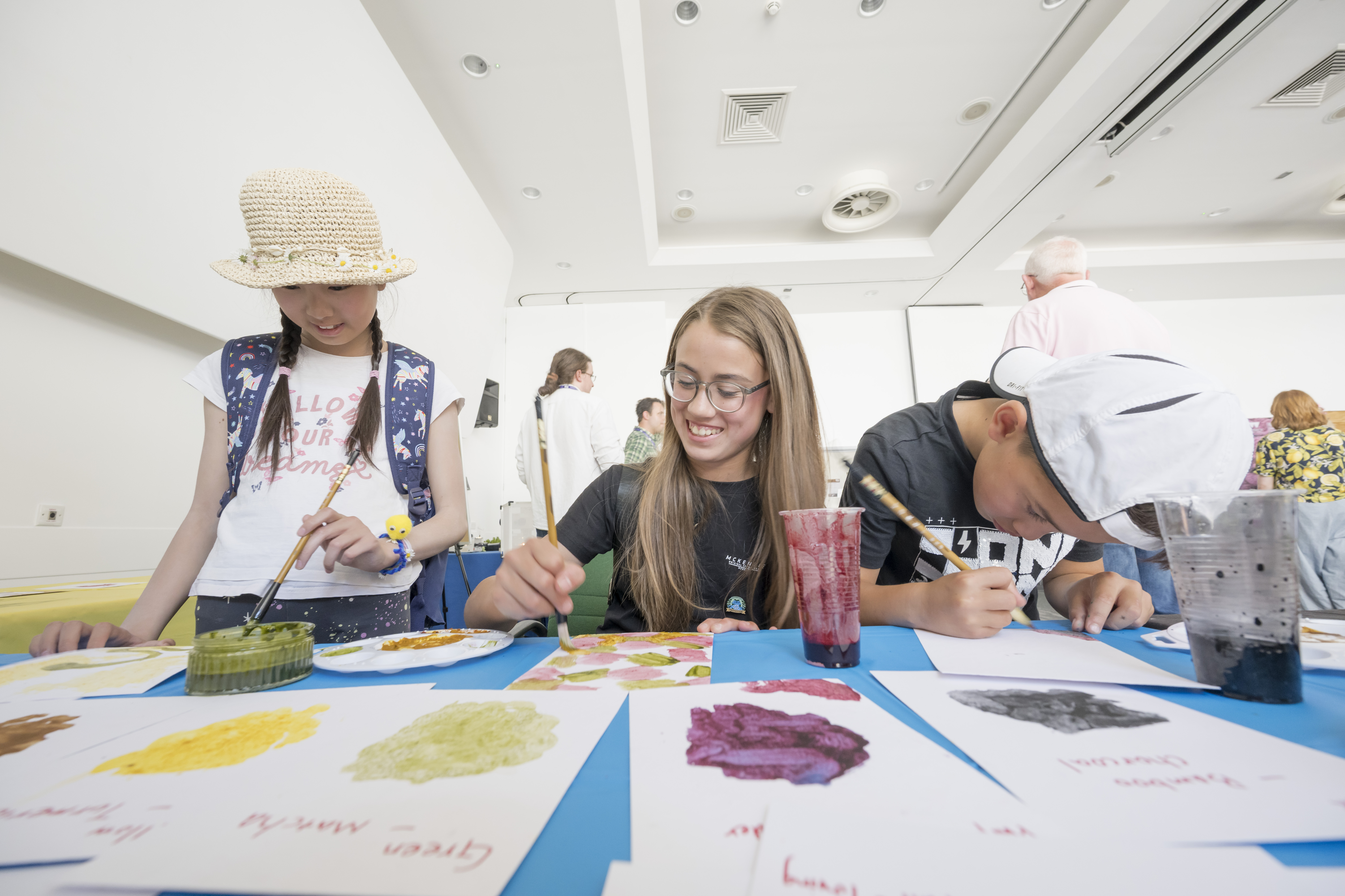 Three children are painting with different coloured paints made from natural materials.