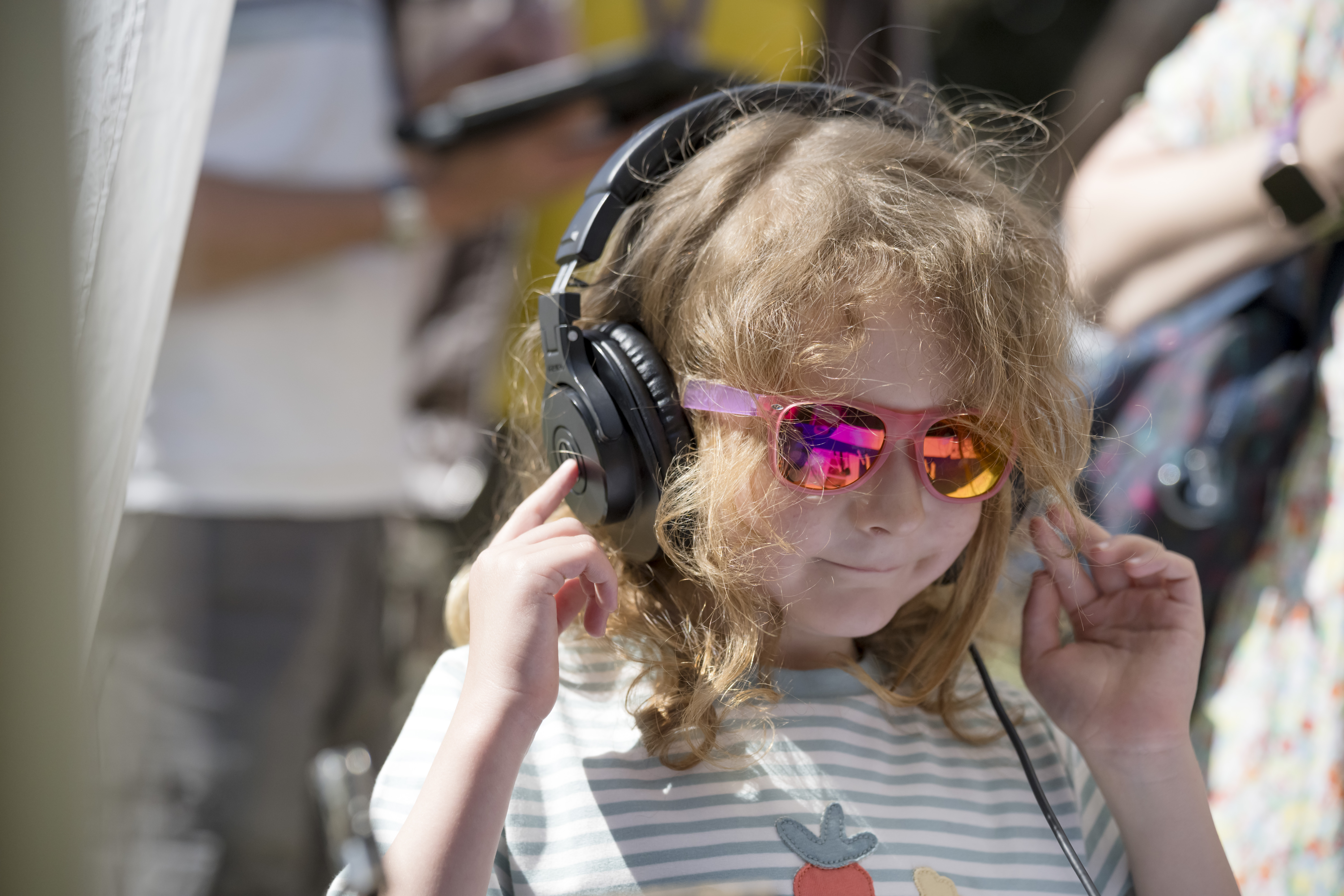 A young boy wearing sunglasses has large headphones over his ears, listening to worms burrowing. He is smiling. 