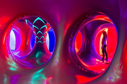 A woman stands inside a colourful art installation with multiple pillars