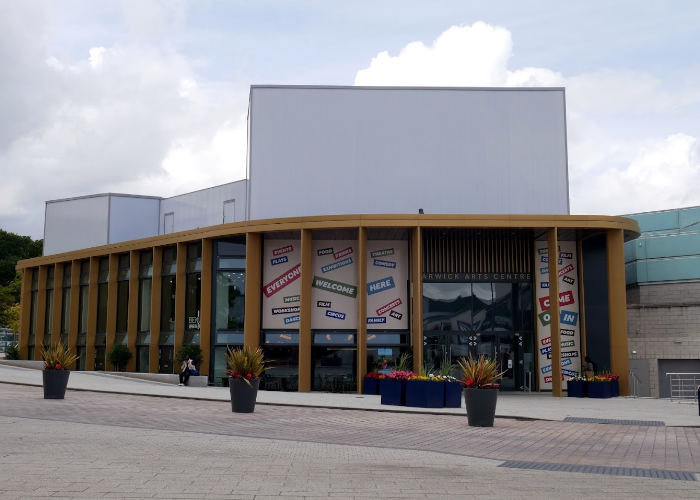 The outside of Warwick Arts Centre with planters filled with flowers on a sunny day