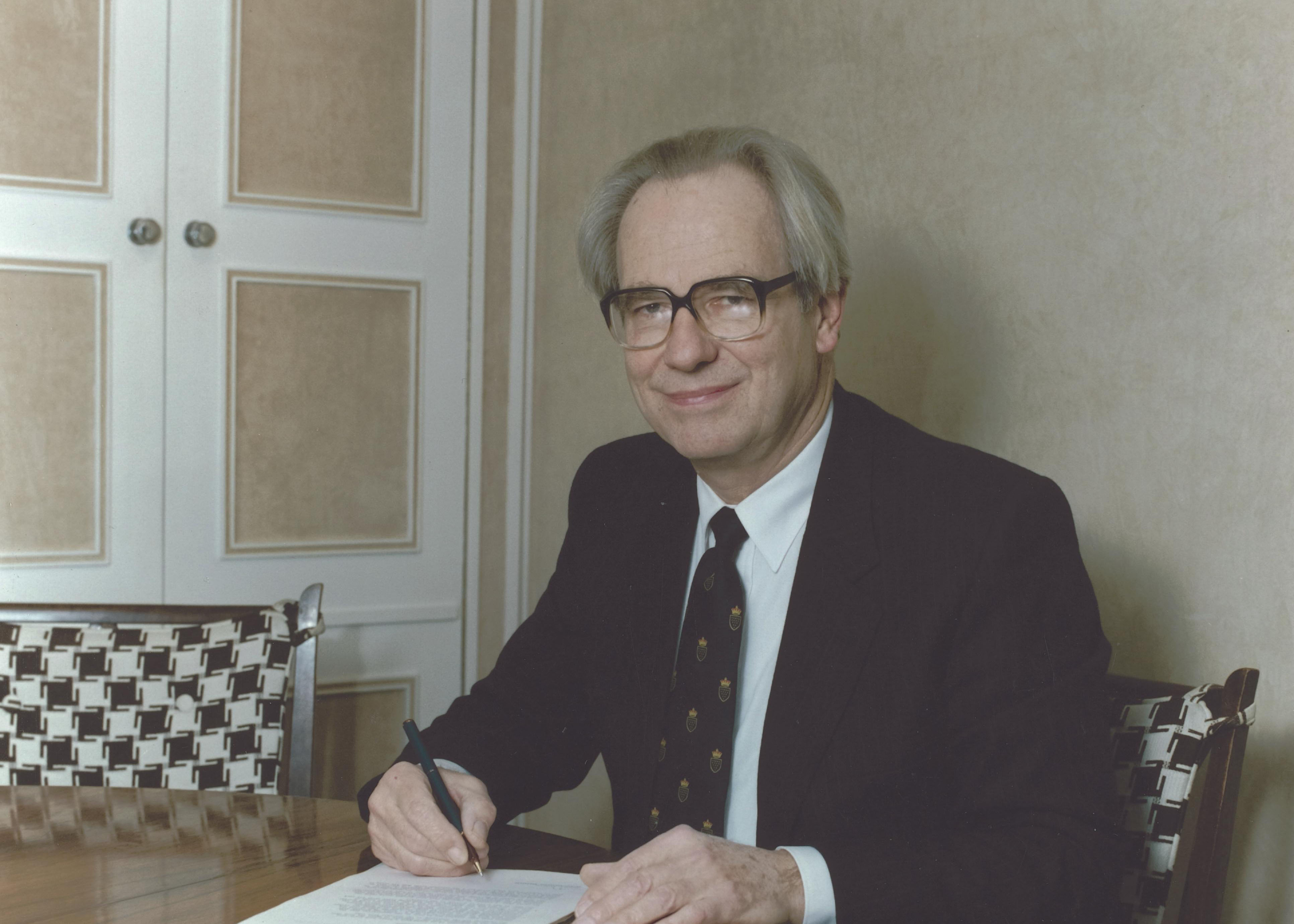 Former Vice-Chancellor of the University of Warwick, Clarke Brundin sits at a desk signing a document