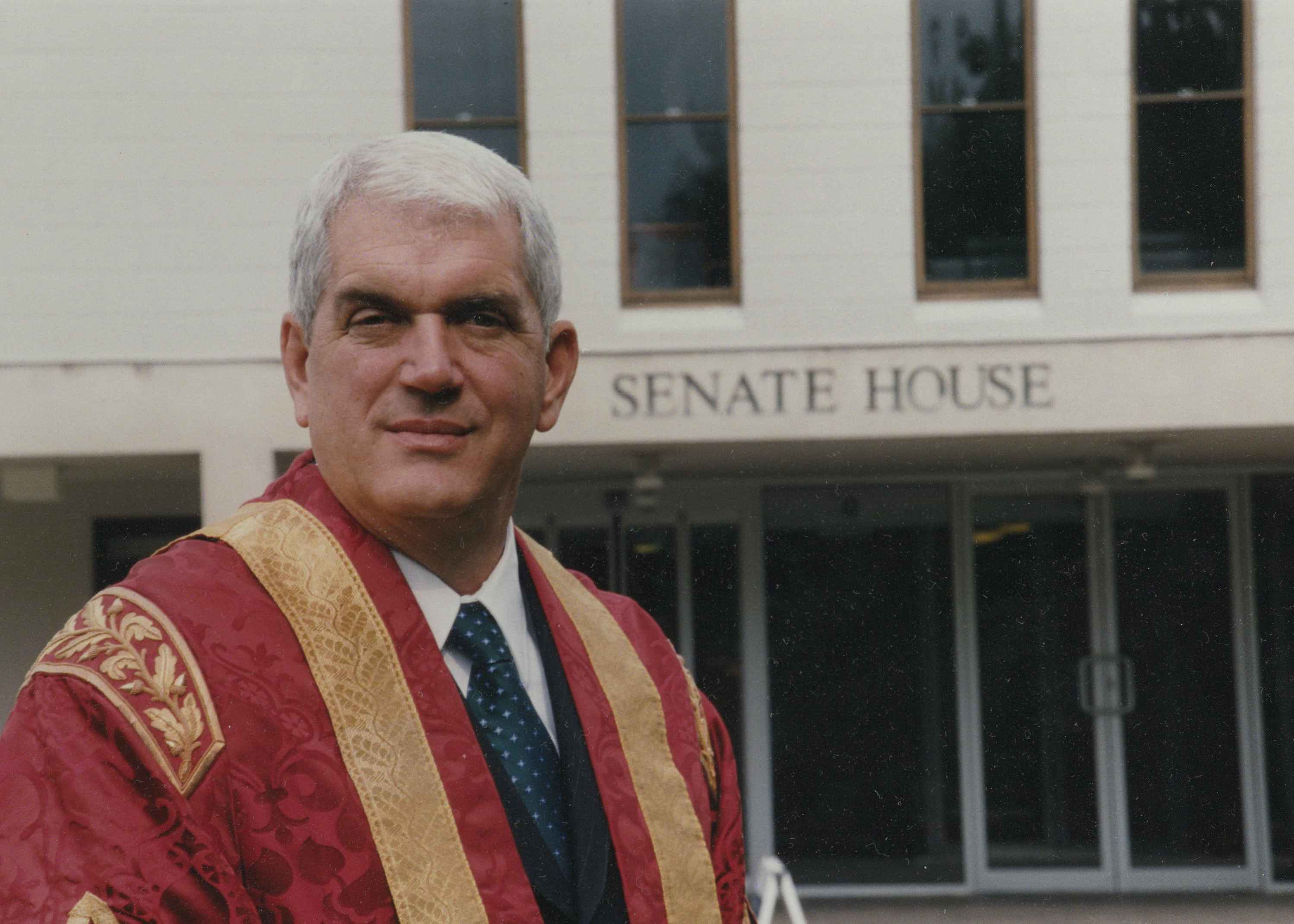 Professor David VandeLinde wearing robes and standing in front of Senate House