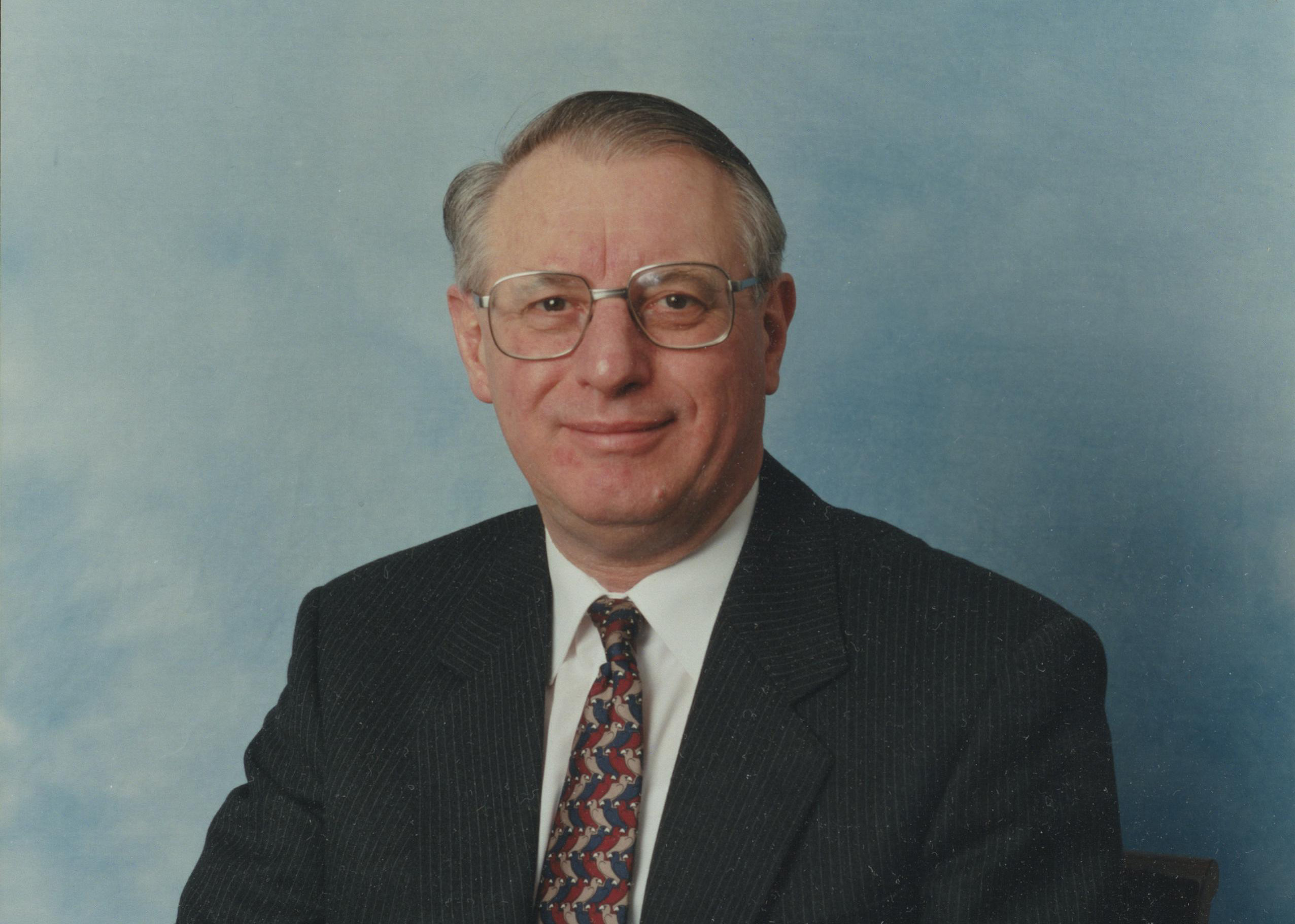 A professional photograph of Sir Brian Follett on a blue background