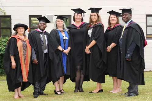 A group of CLL graduates in their graduation robes smiling at the camera