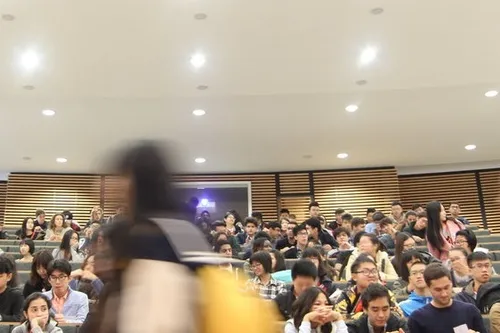 A group of International students sitting in a lecture theatre with one student walking quickly past the camera in a blur