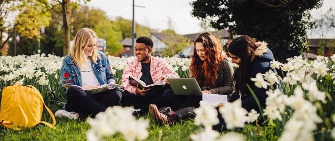 Students sitting in a grassy area working on laptops or reading books