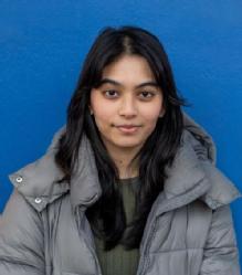 Image is a head and shoulders photo of student volunteer Modhurima Islam wearing a grey jacket against a blue background