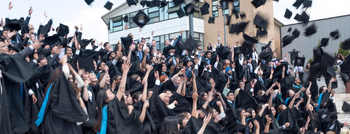 A large group of University of Warwick alumni throwing their caps into the air in celebration.