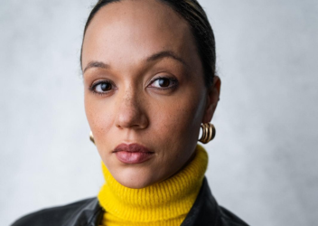 Erin looks seriously at camera in a yellow polo neck