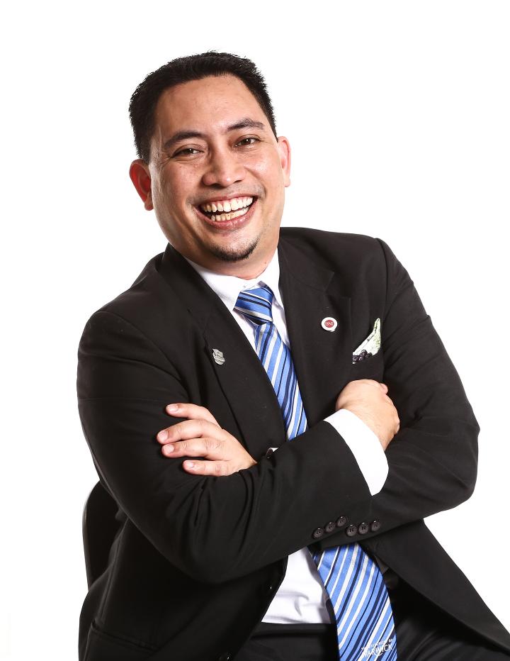 Ed folds his arms in a suit and smiles at camera