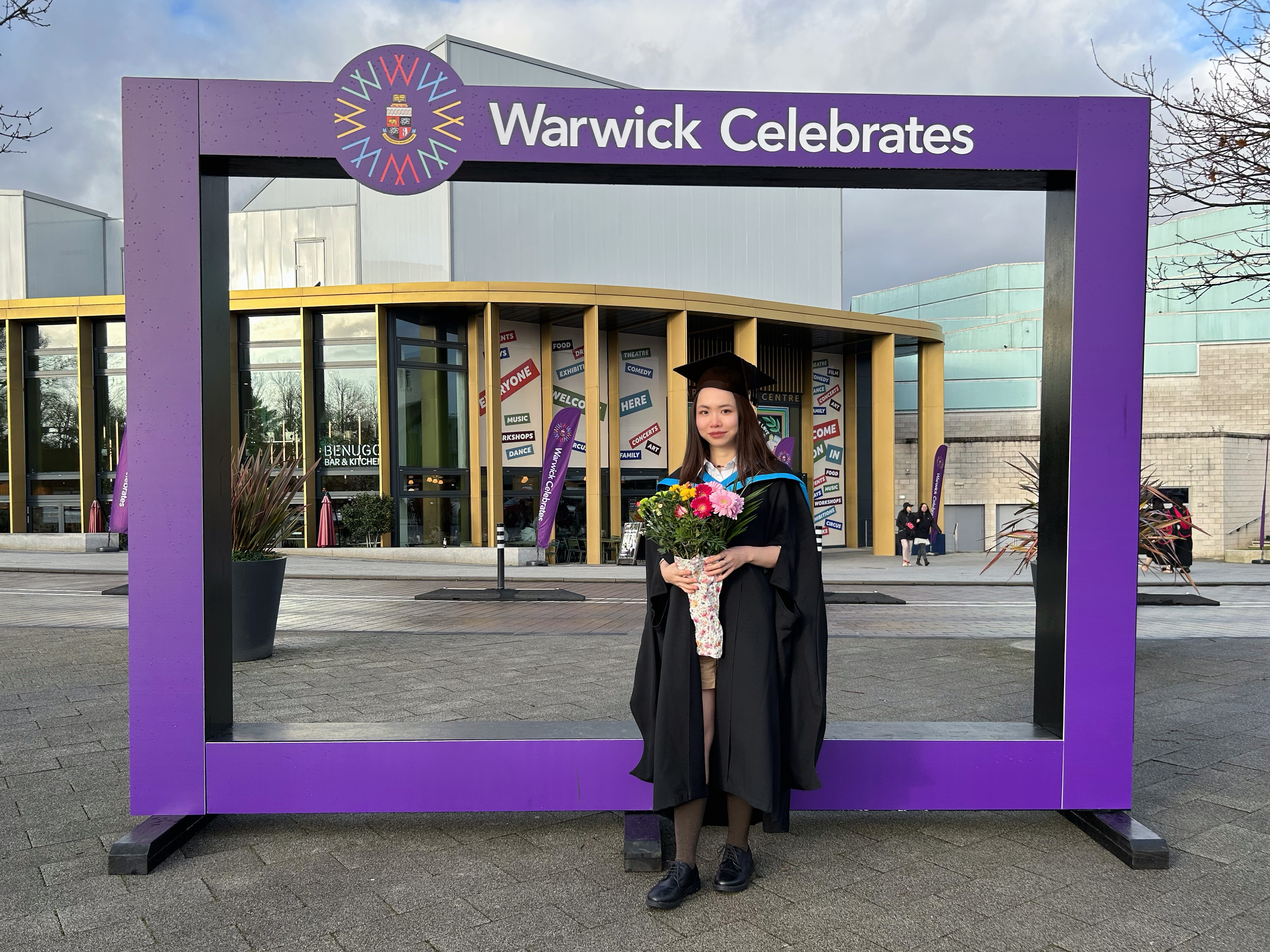 Alex at her graduation ceremony holding a bunch of pink roses
