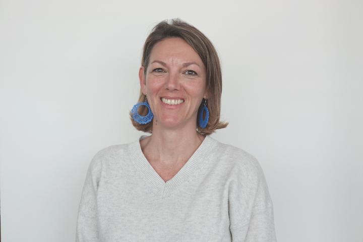 Anneke wears an off-white jumper and circular blue earrings against a white background