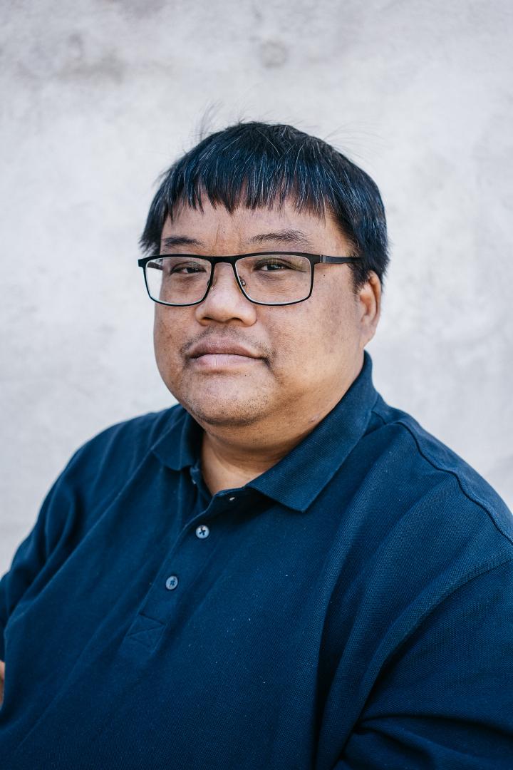 David looks directly at camera with glasses and a blue polo neck