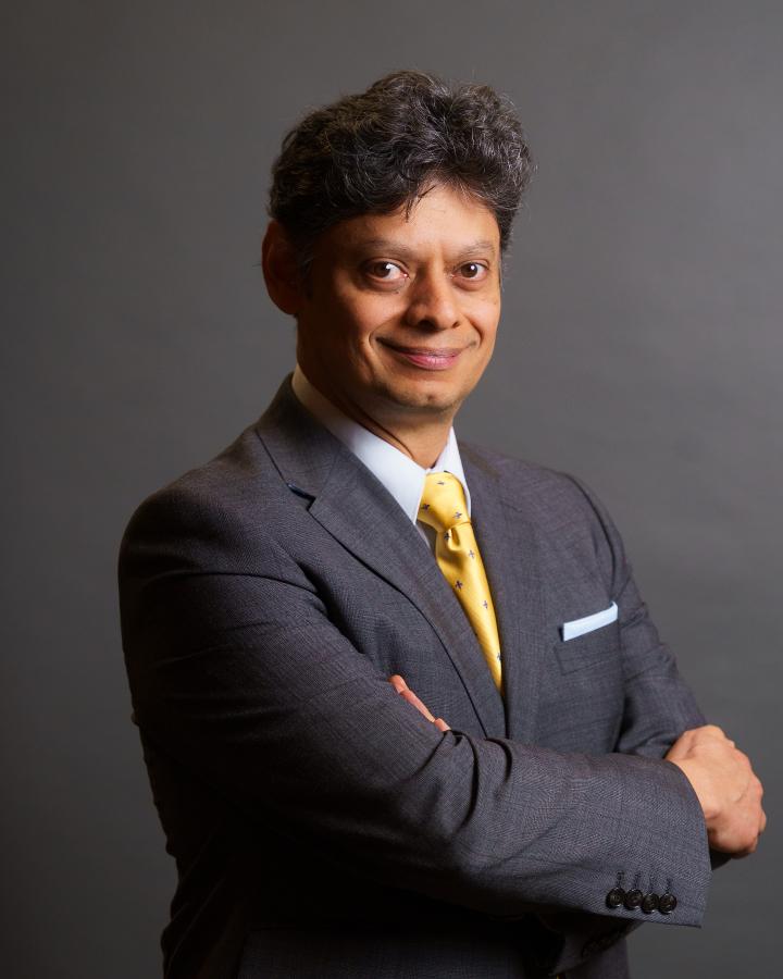 David wears a dark grey suit with yellow tie and smiles at camera