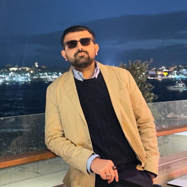 Dhyeykumar wears sunglasses and leans against a glass balcony looking at camera
