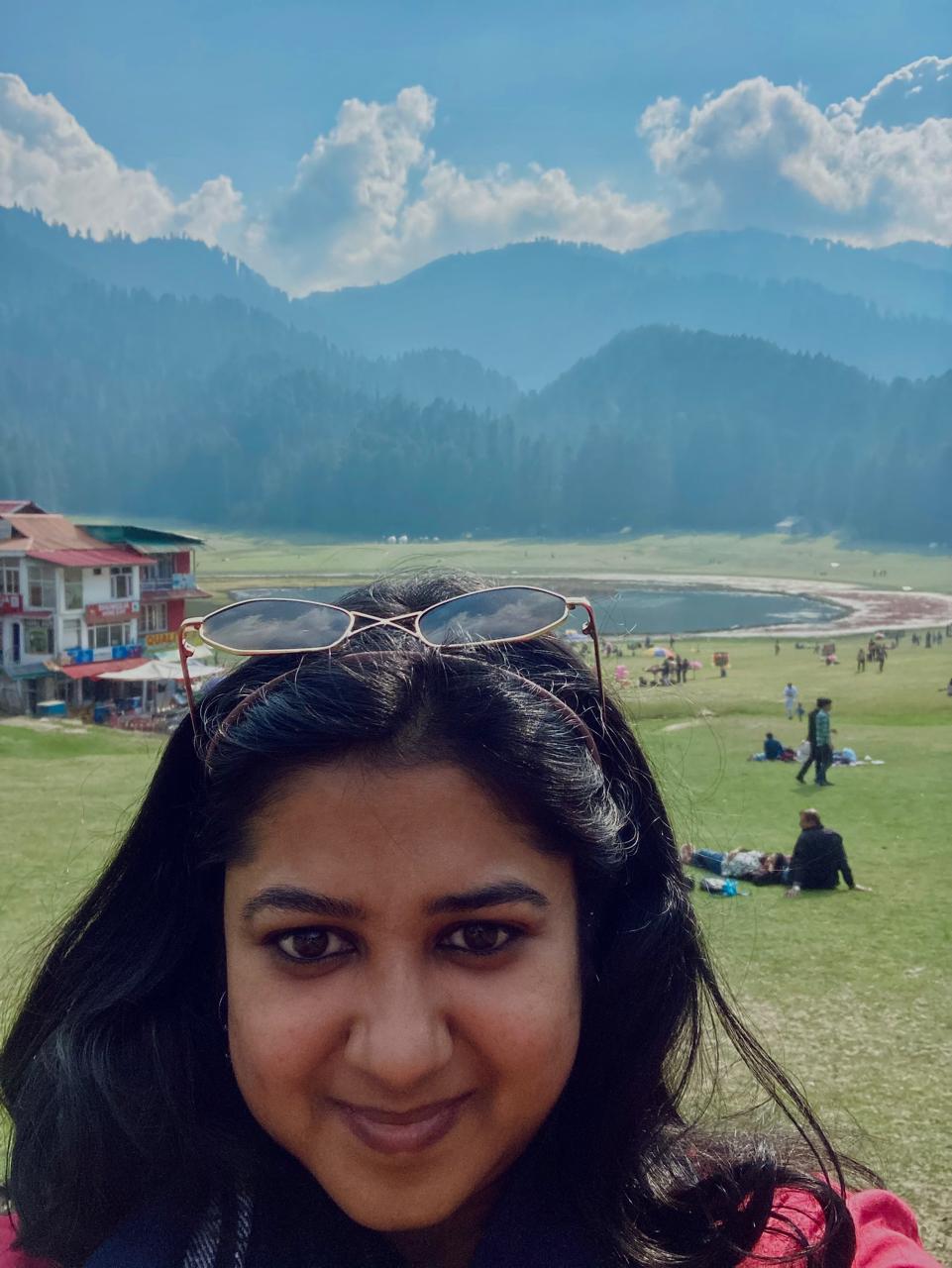 Divya stands in front of a beautiful mountainous landscape.