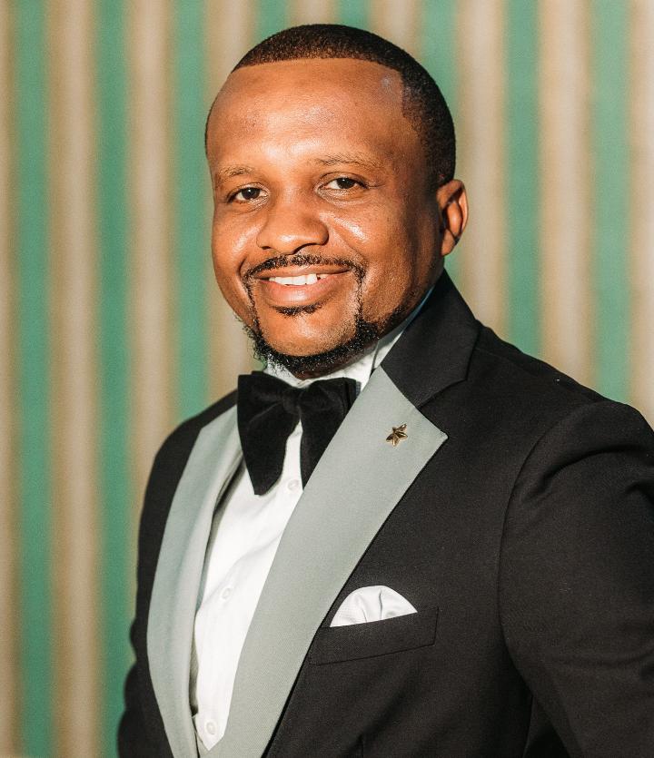 Kelvin wears a grey lapel black suit and bow tie
