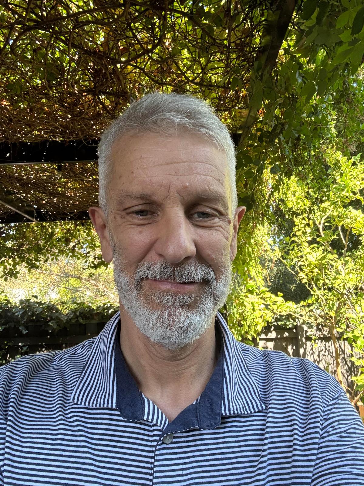 Nick in a blue and white striped shirt with a background of green trees