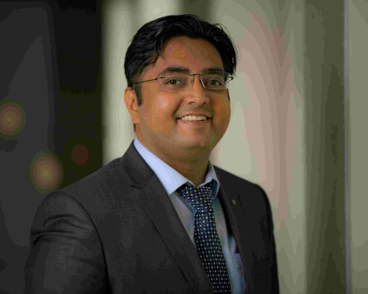 Palak in a grey suit with blue spotty tie smiles at camera
