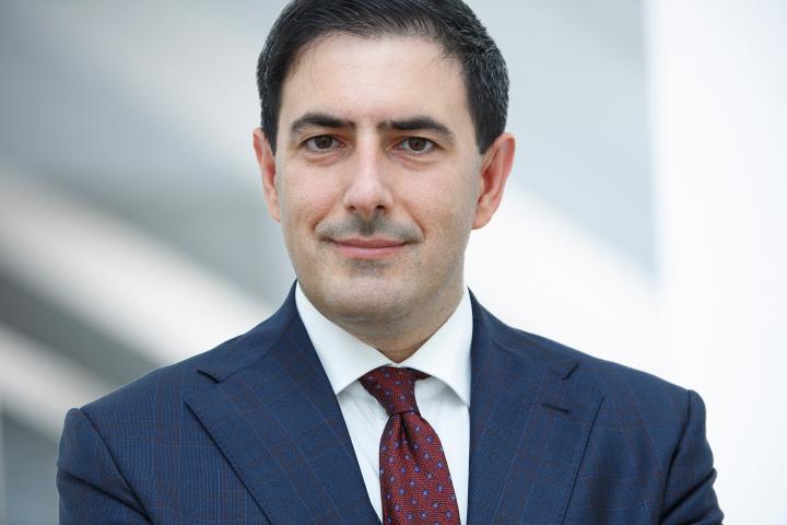 Philip looks to camera in a blue suit and red tie