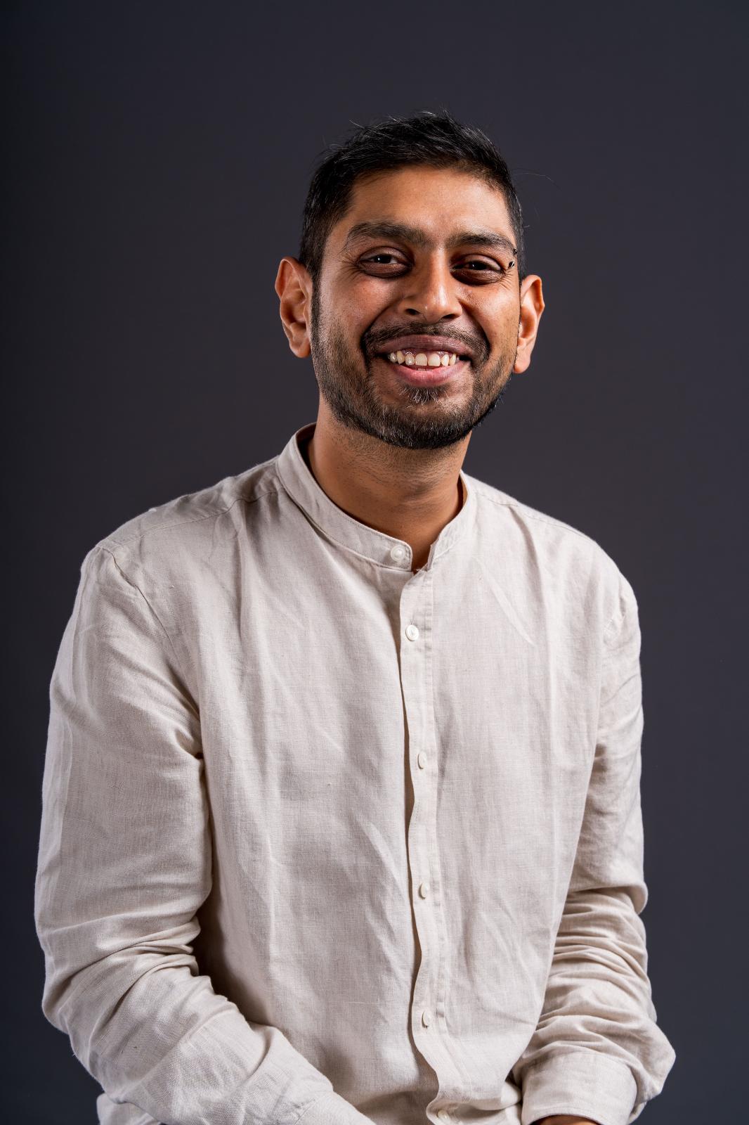Preet wears an off-white shirt against a deep grey background