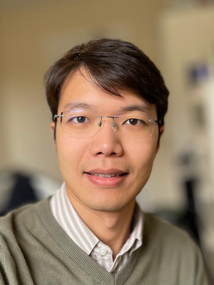 Qing has glasses and a green jumper