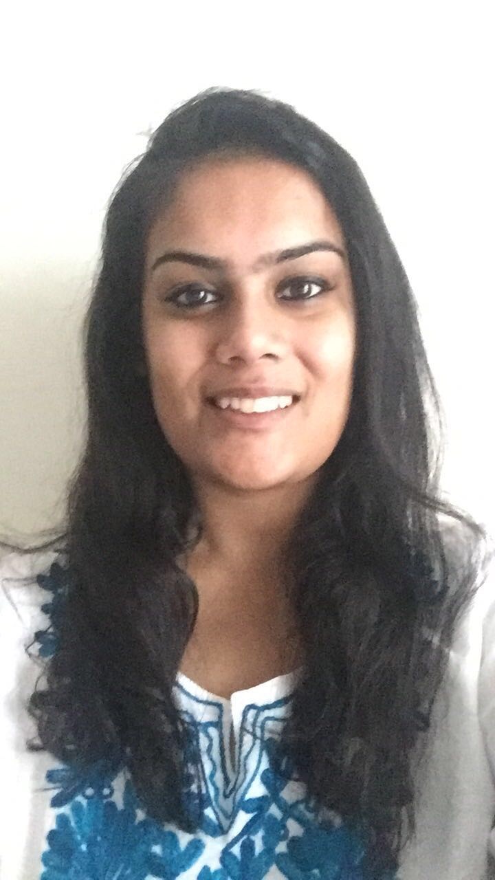 Ragini smiles at camera. She has long dark hair and a white and blue top on