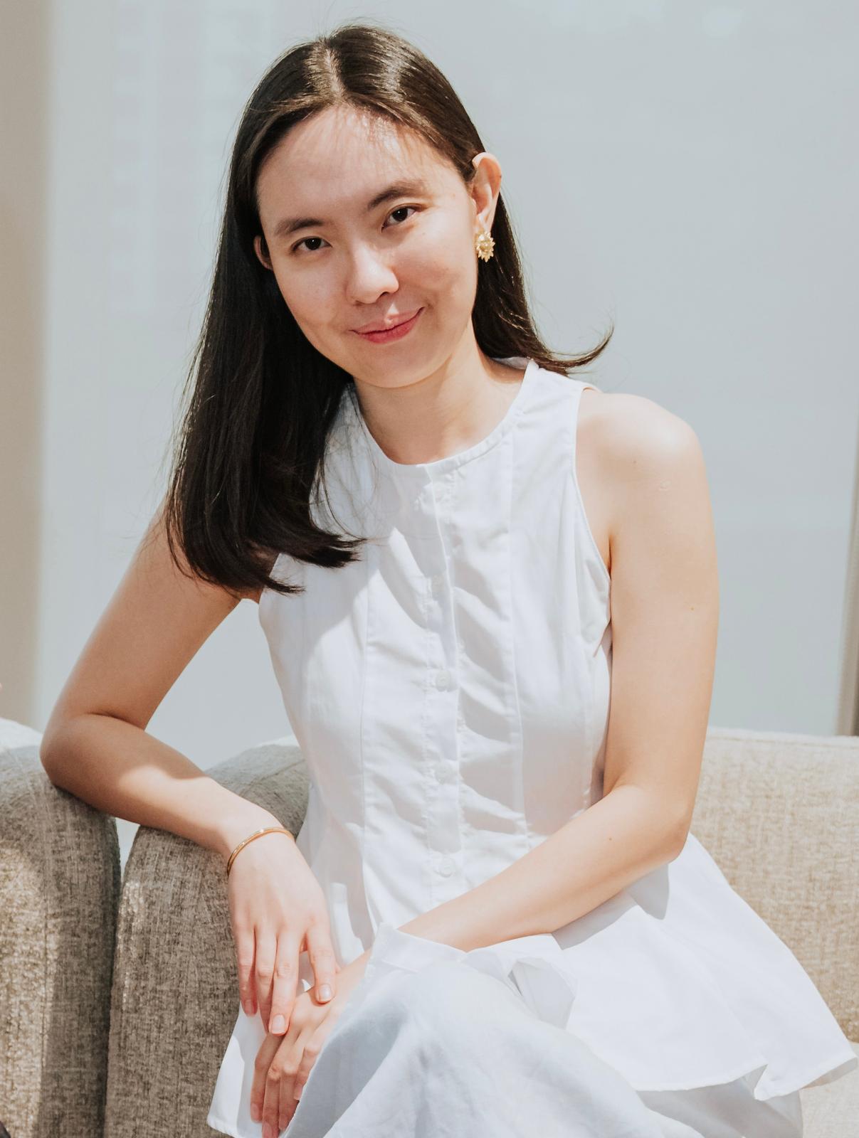 Wenfei smiling, sitting on a sofa in a white dress