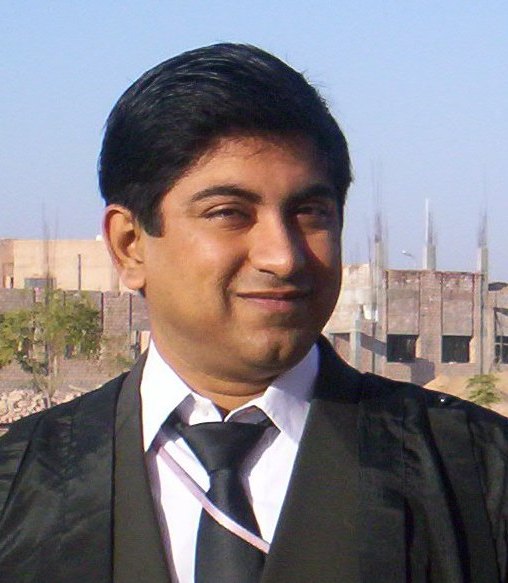 Souvik stands in a black suit and tie with a blue sky behind him