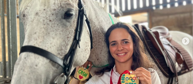 Noor holds up a medal beside her horse