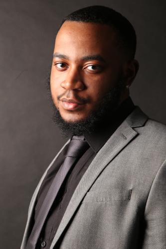 Headshot of Guilio in a grey suit with a grey tie and black shirt