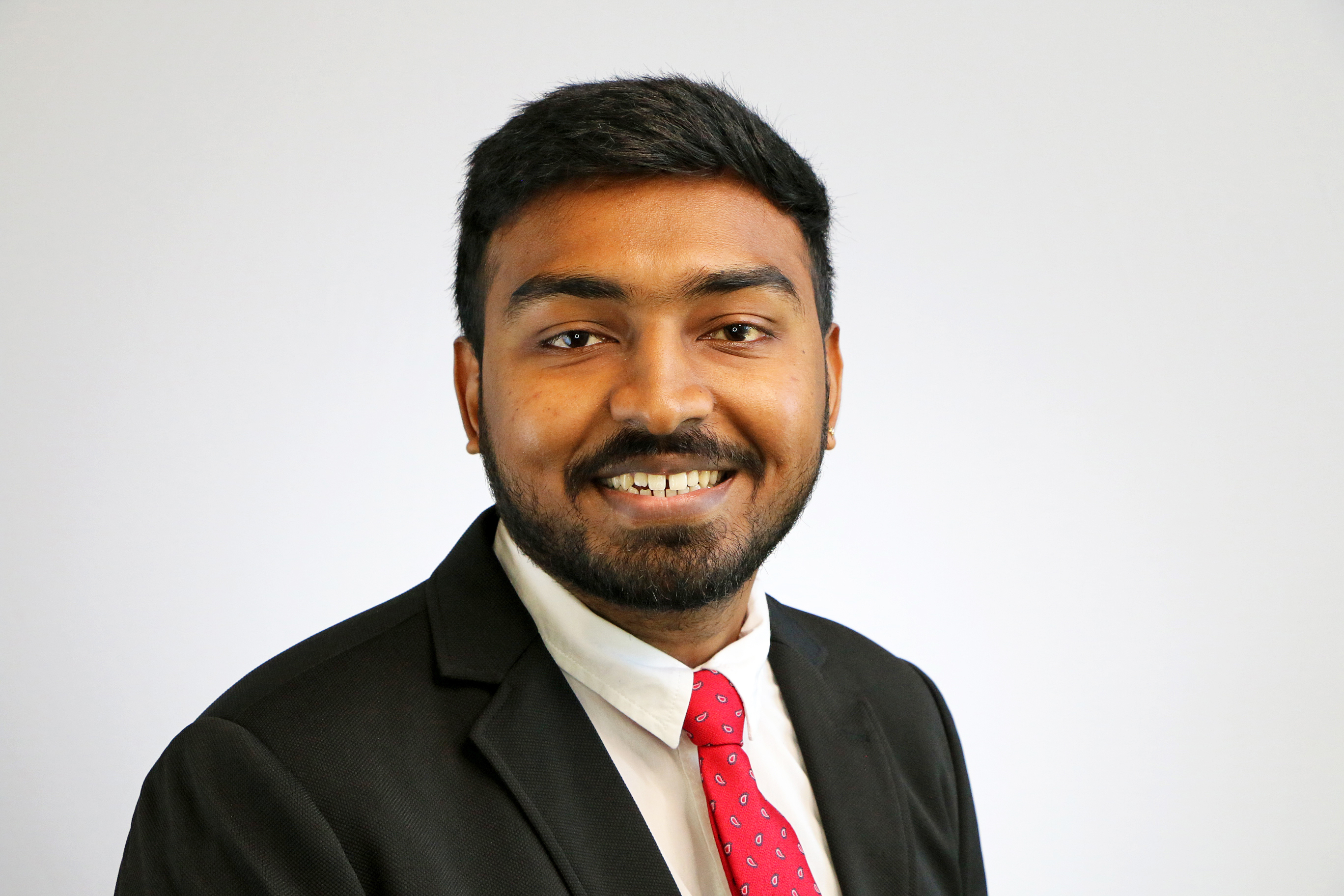 Abilash smiles in a suit with a red tie