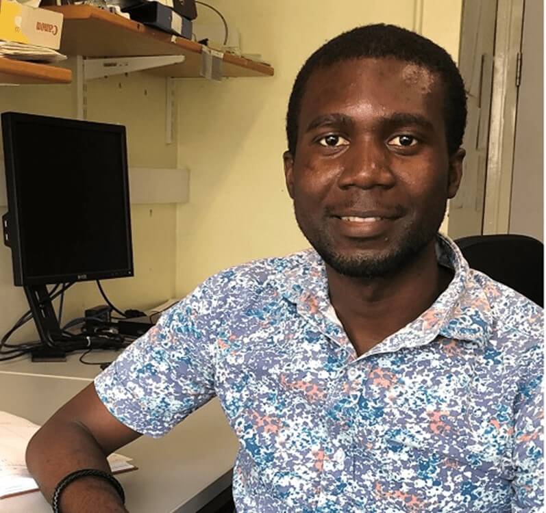 Samson Oladeji sitting next to a computer and wearing a flowery shirt