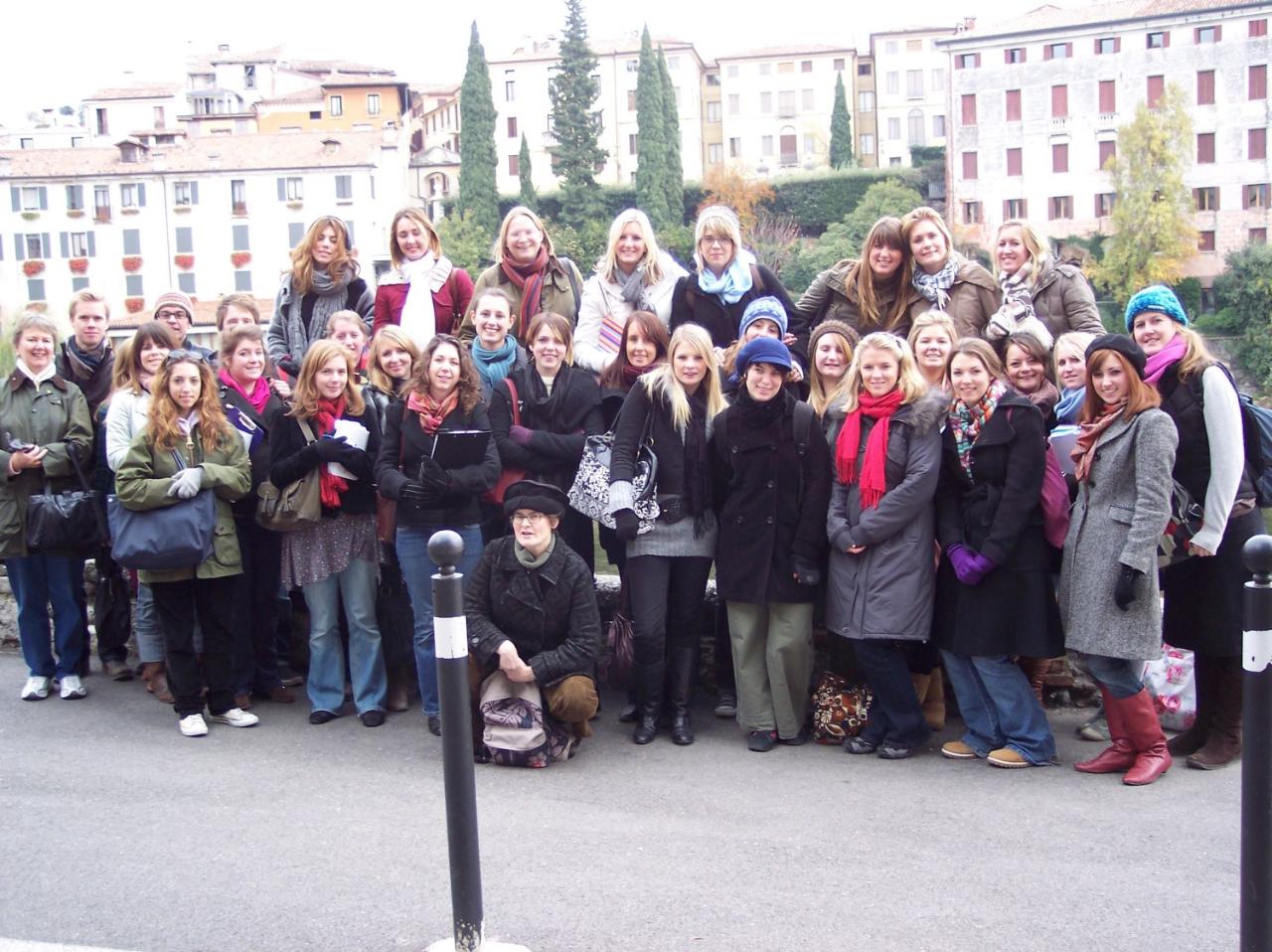 A large group of students all posing for the photo with white buildings and trees behind them.