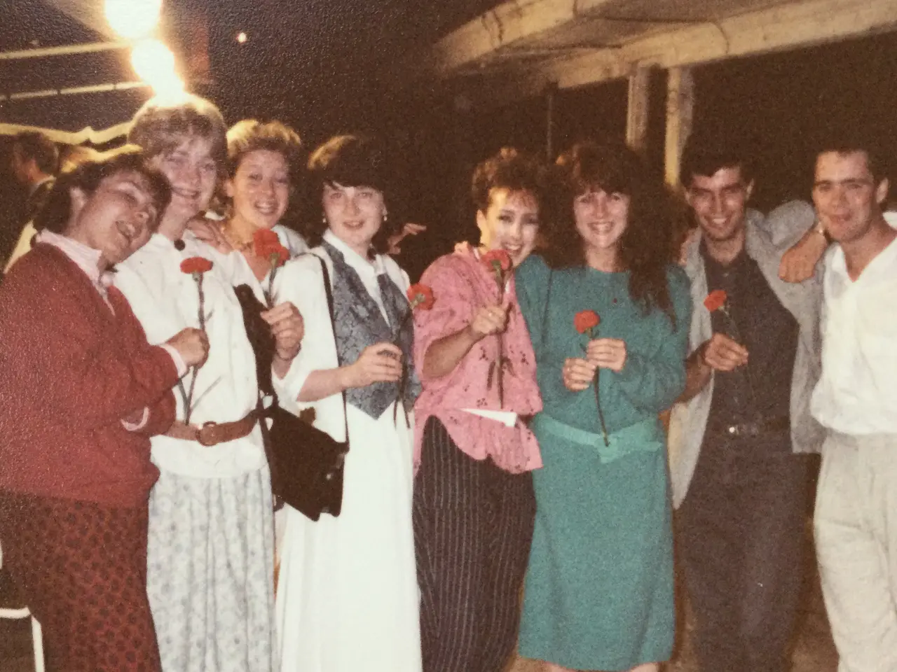 A group of people all smiling at the camera, some holding red flowers