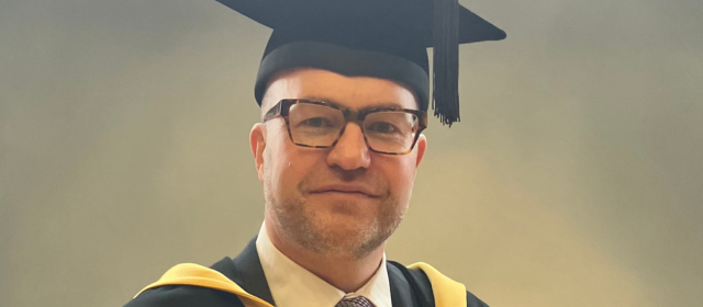 Jon in his graduation robes with a yellow hood