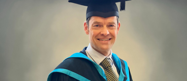 Paul in his graduation robes with a blue hood