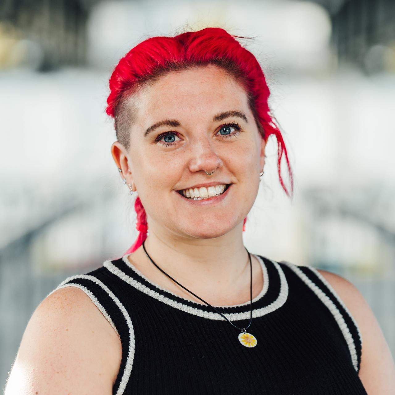Charlie has her bright red hair tied back and is wearing a black, white trimmed, vest top