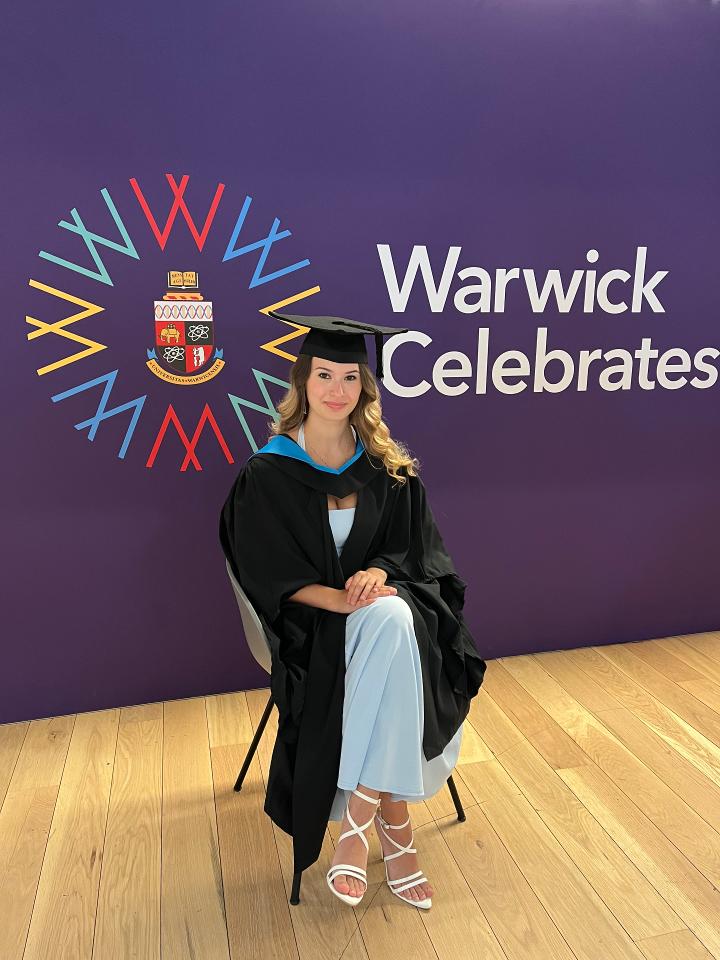 Julia sits in front of a graduation backdrop in her cap and gown