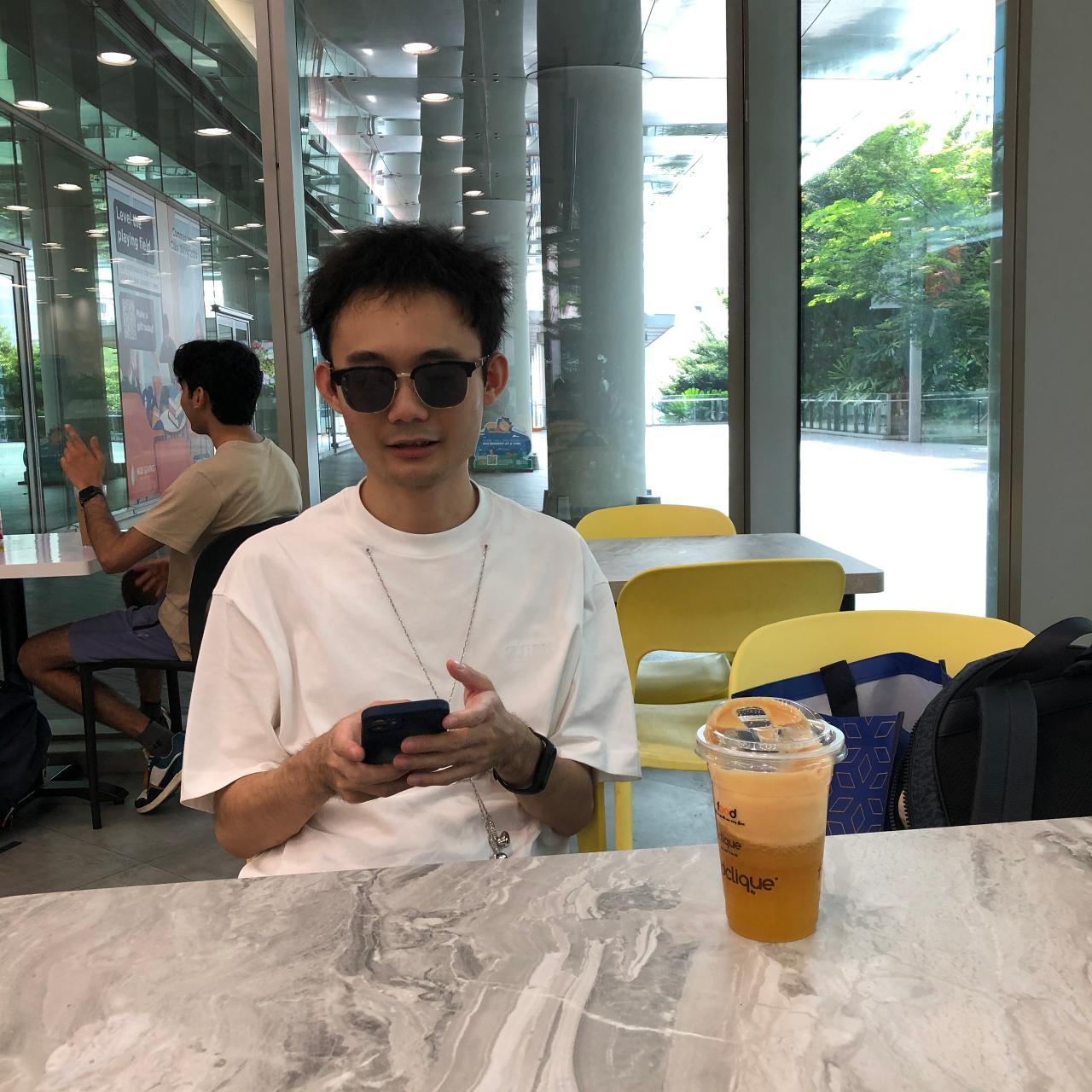 Junbo looks at his phone in a cafe, wearing sunglasses