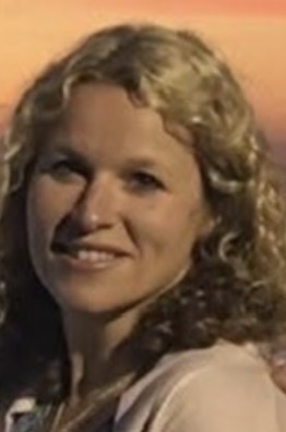 Kristina has blonde curly hair and stands before a sunset