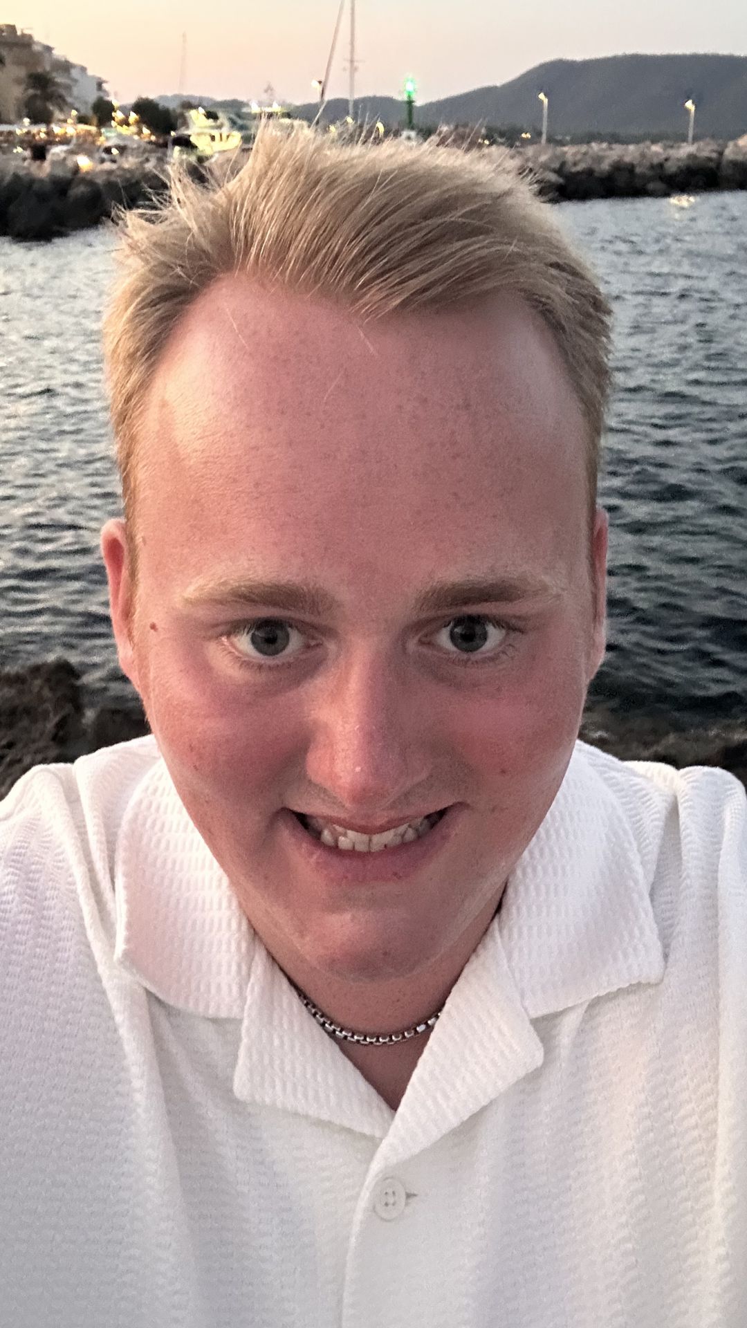 Leon in a white shirt with a harbour behind him