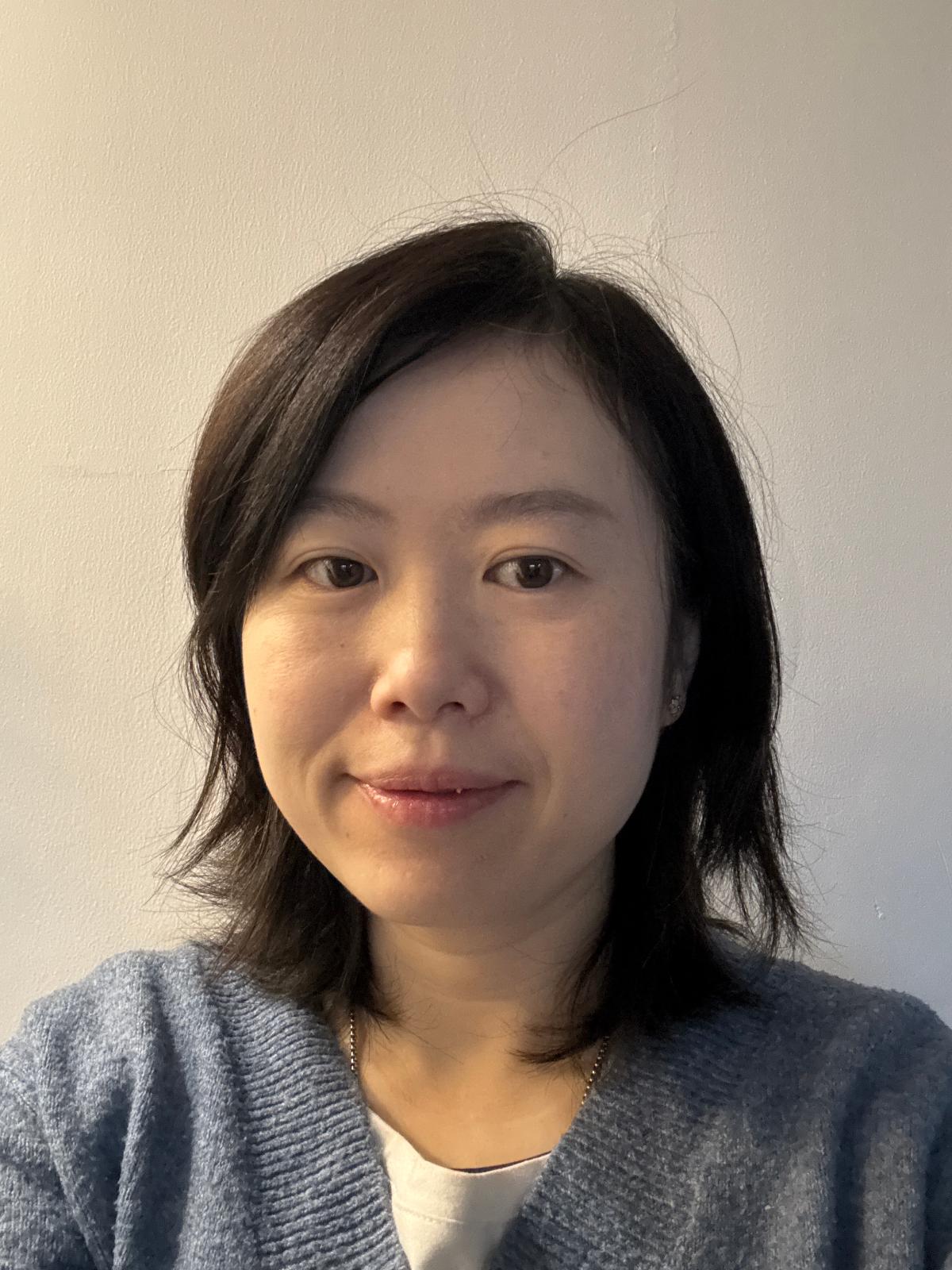 Li smiles at camera in a grey-blue jumper