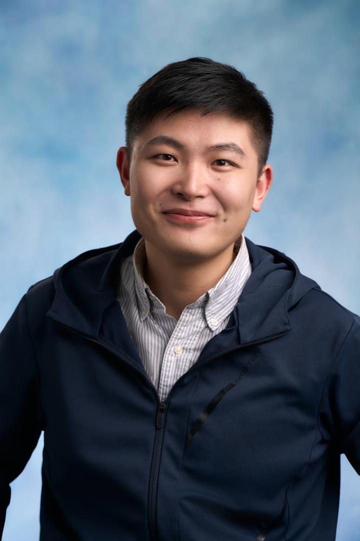 Pengyun in a shirt and jacket smiling at camera with a blue sky behind him