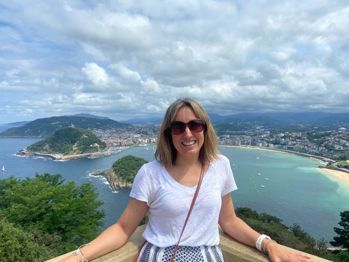 Rosalind on holiday smiling at camera wearing sunglasses overlooking a bay