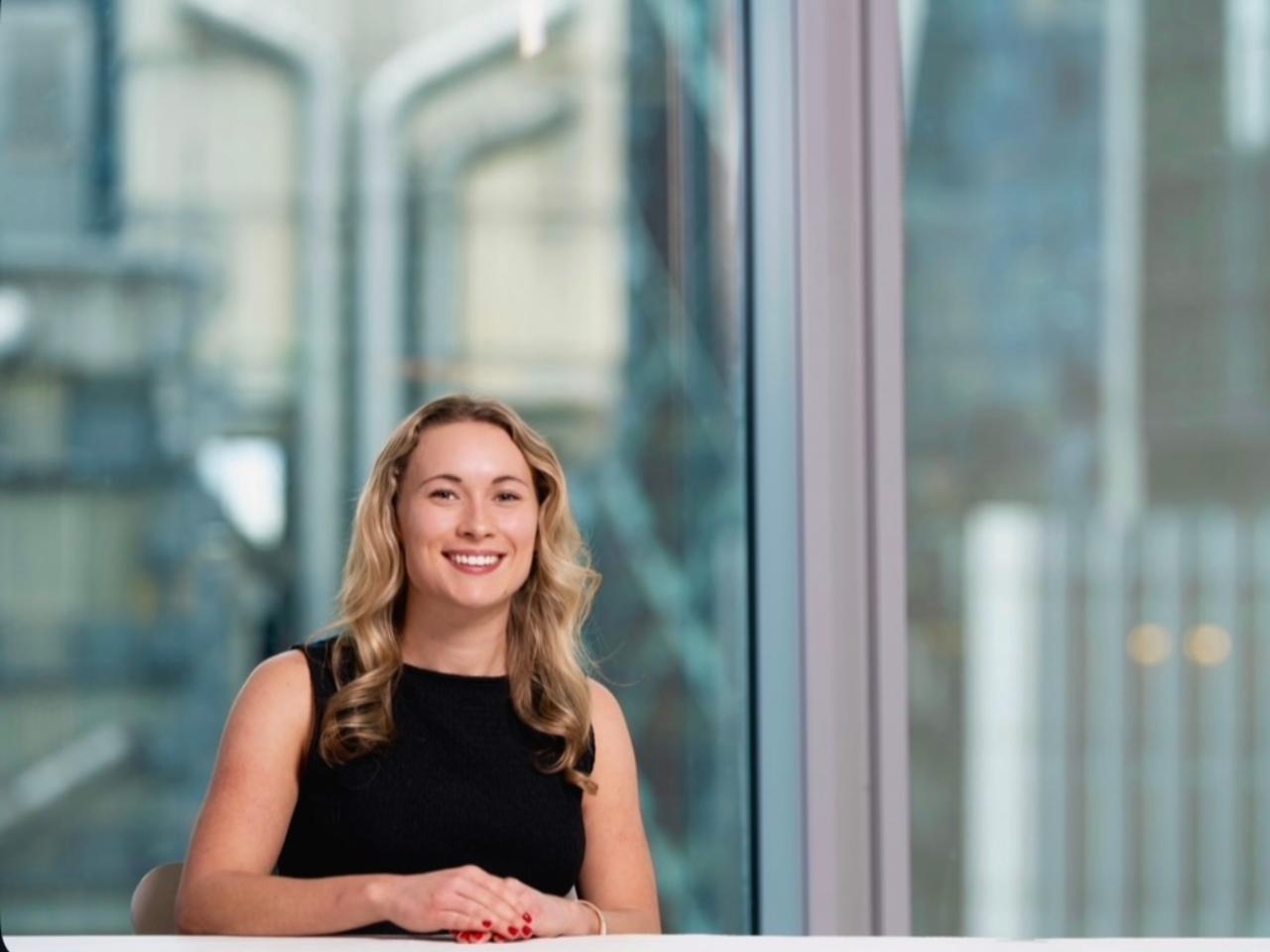 Sophie sits facing camera with long glass windows in her background
