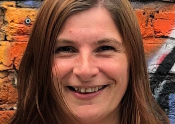 Rebecca smiling at camera with a colourful orange mural behind her