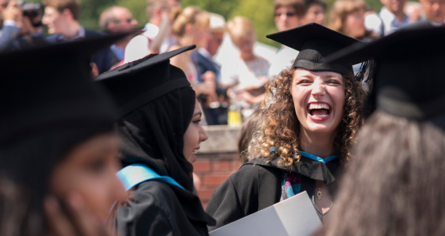 A graduate smiles at the camera from within a crowd