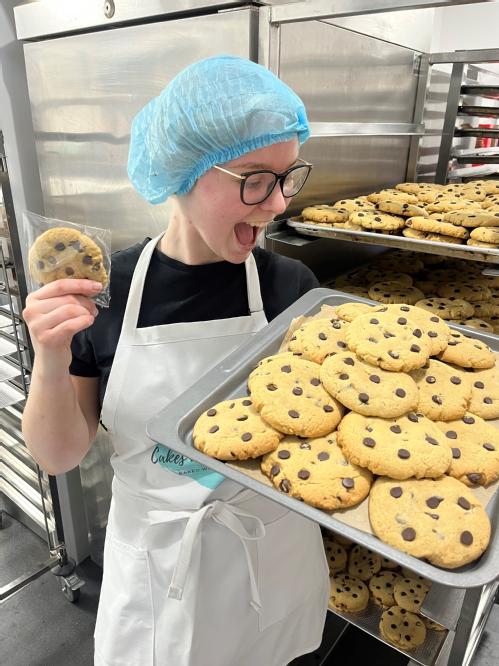 Immi in chef's jacket wearing a blue hairnet holding a tray of cookies
