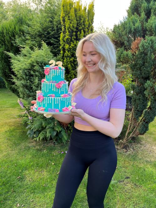 Immi outside holding a three tiered cake with blue icing 